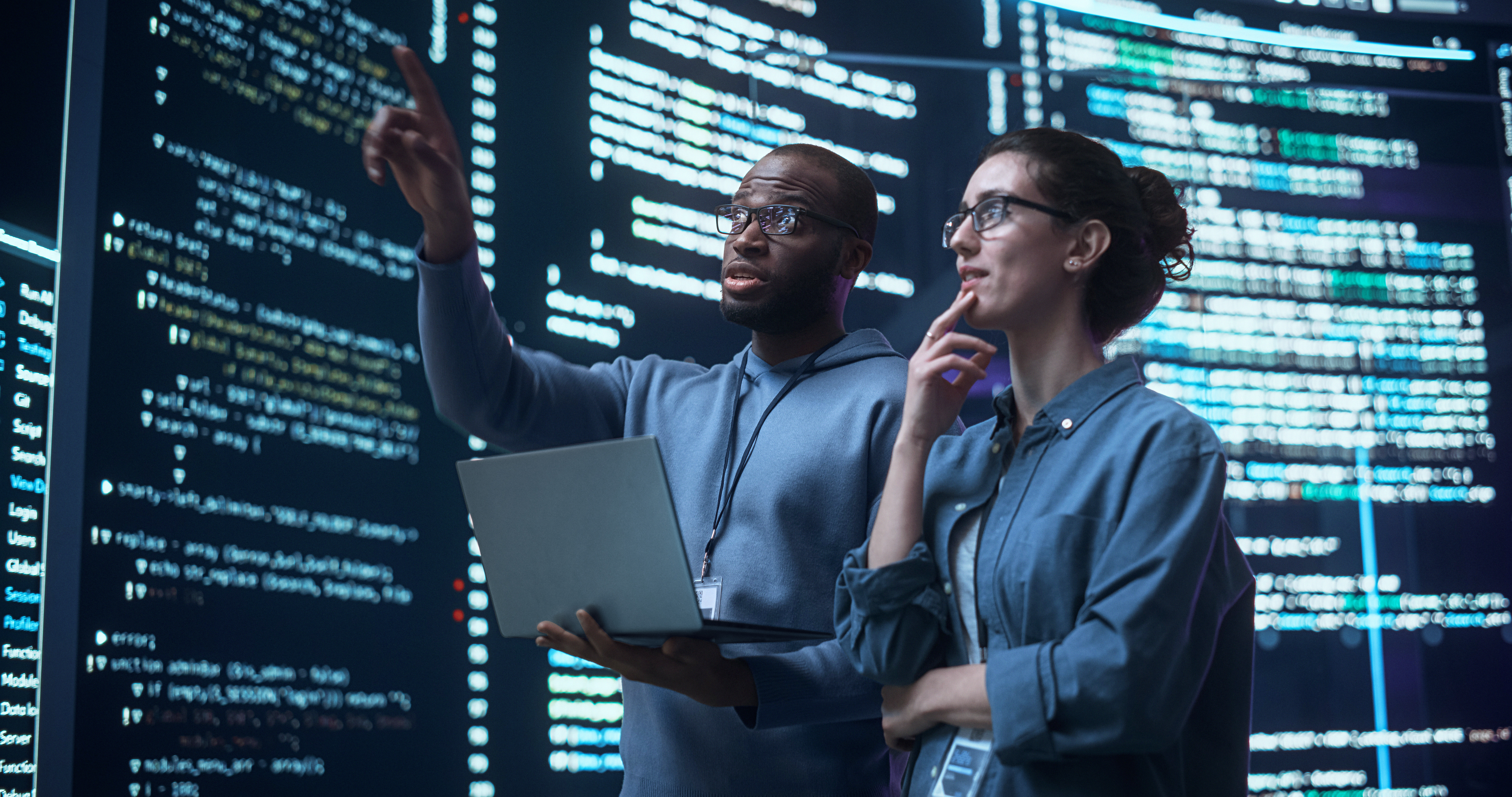 Man and woman standing in room pointing at screens