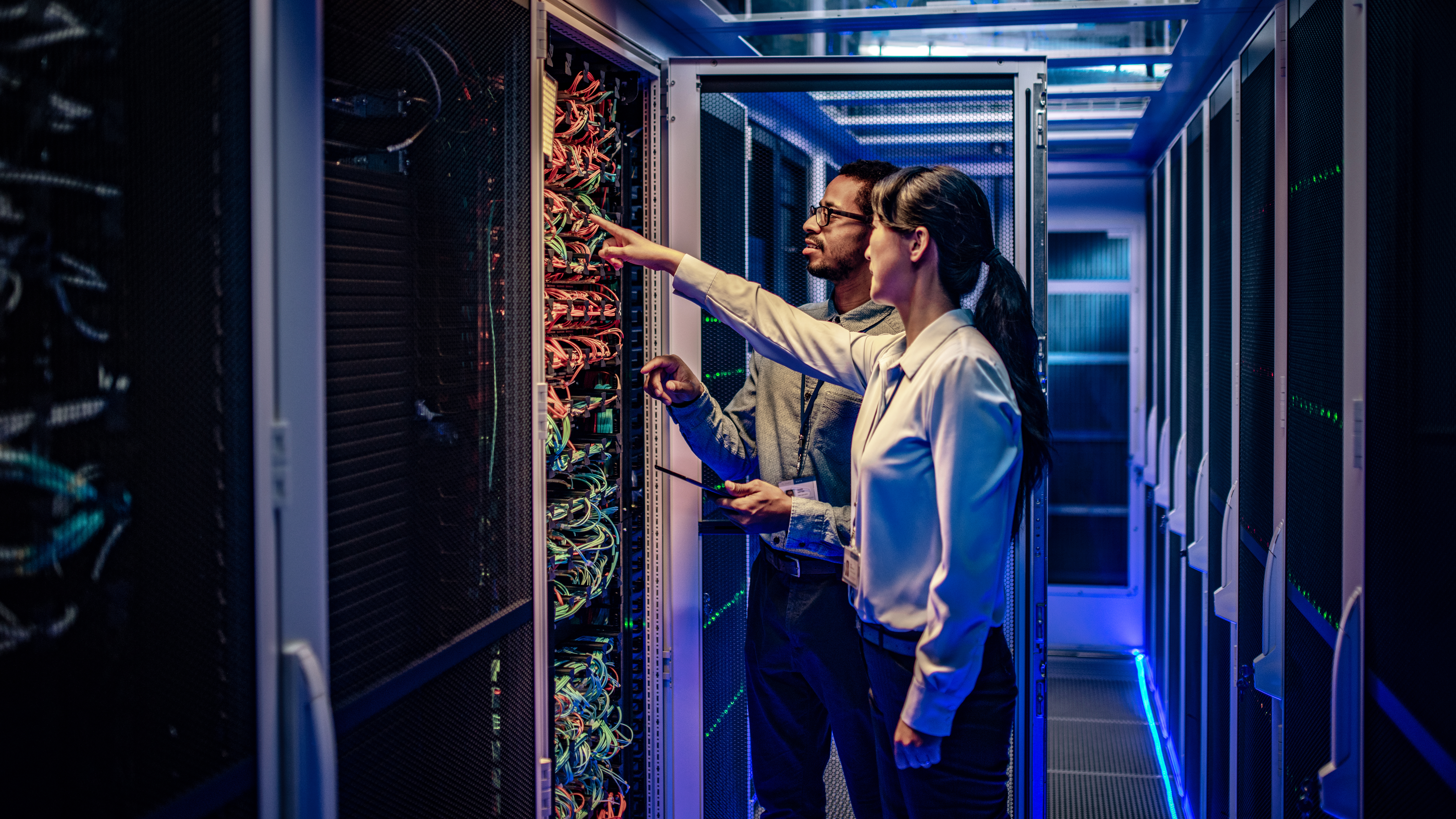 A man and woman inspecting a server rack in a data center.