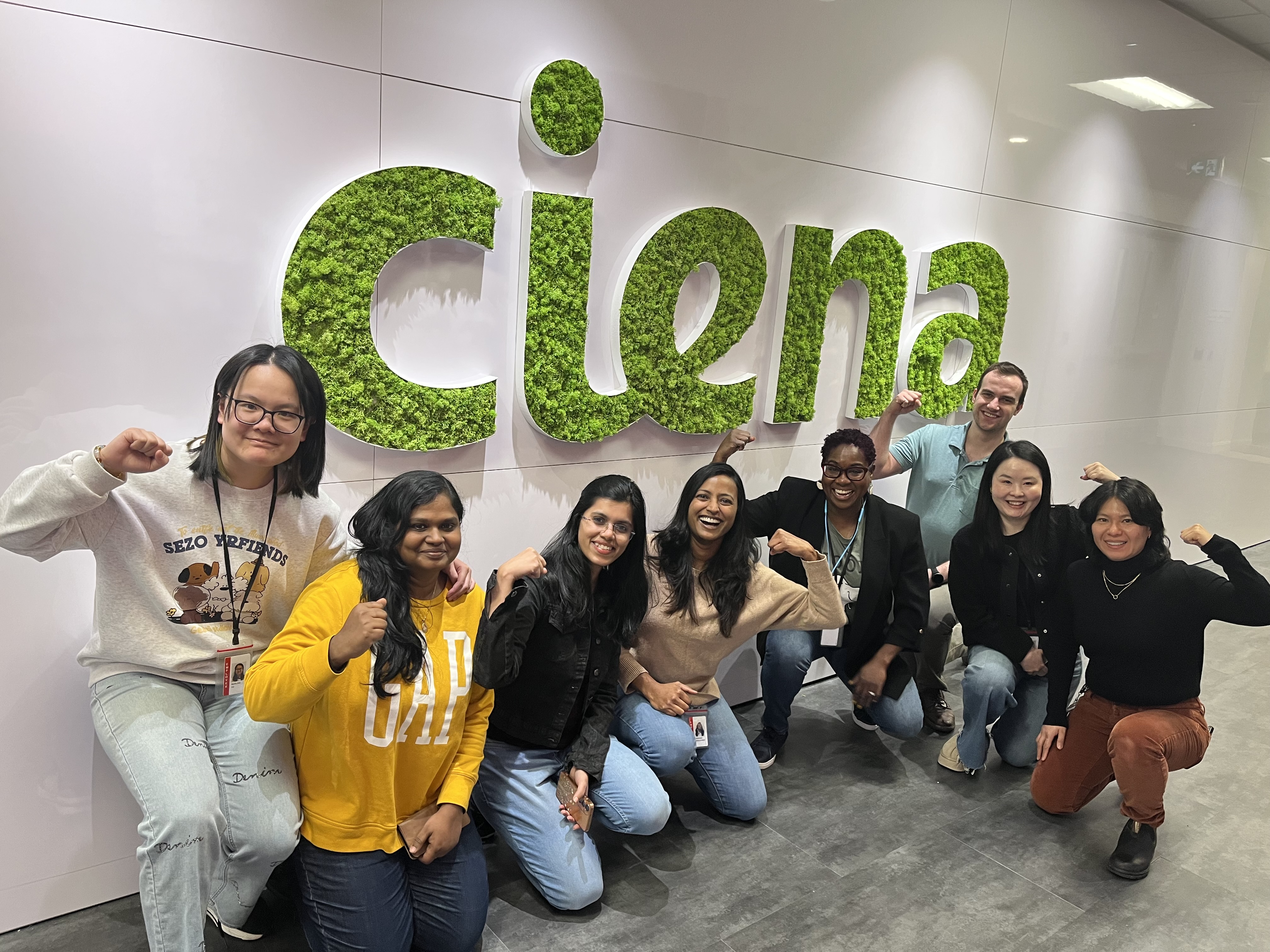 Group of people flexing muscles posing in front of wall with Ciena logo