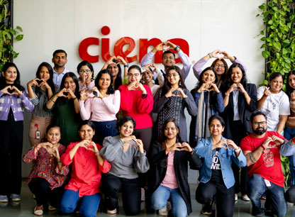 Group of Ciena employees posing in front of logo and making heart symbol with hands
