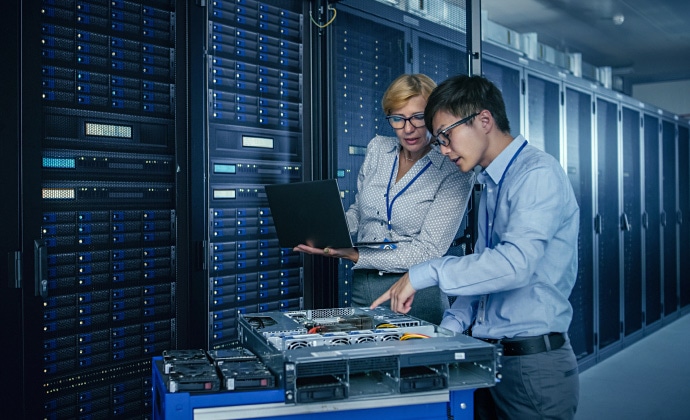a man and a woman standing in a data center looking at a laptop