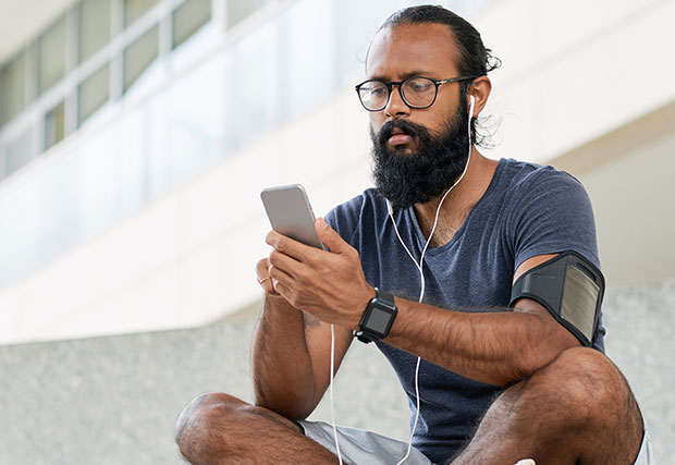 An image of a man sitting and using a mobile device, engrossed in the digital world. He is holding the device in his hands, interacting with the screen, symbolizing the ubiquity and seamless integration of mobile technology in our daily lives.