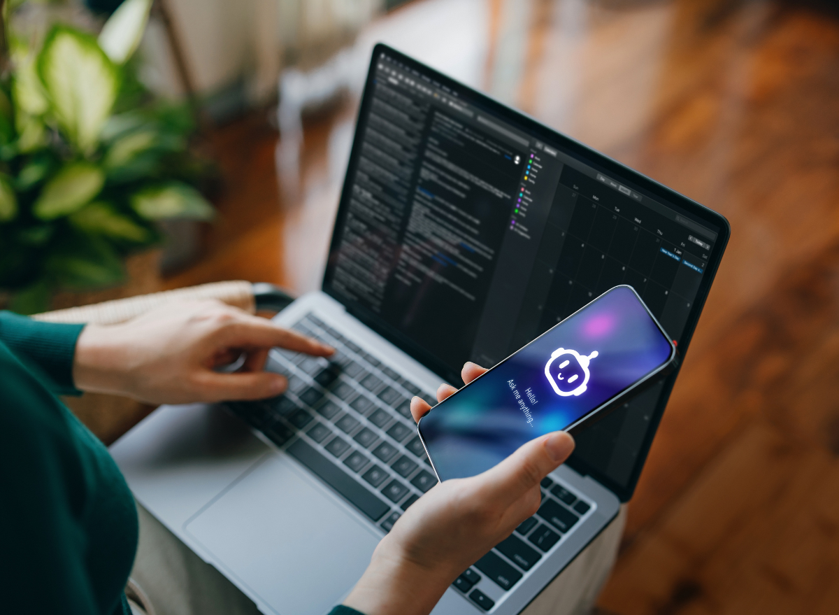 Open laptop with person holding mobile device and using an AI chatbot